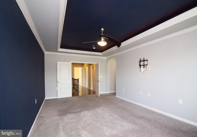 unfurnished bedroom featuring arched walkways, a raised ceiling, baseboards, ornamental molding, and carpet flooring