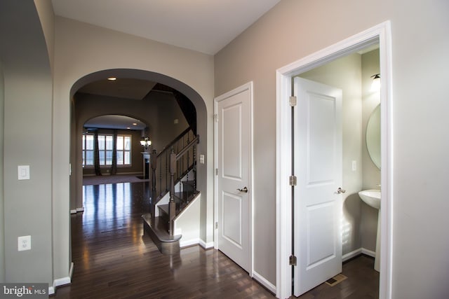 hallway with stairs, arched walkways, baseboards, and dark wood-type flooring