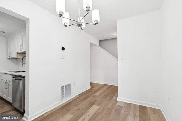 unfurnished dining area with a sink, a chandelier, light wood-style flooring, and baseboards