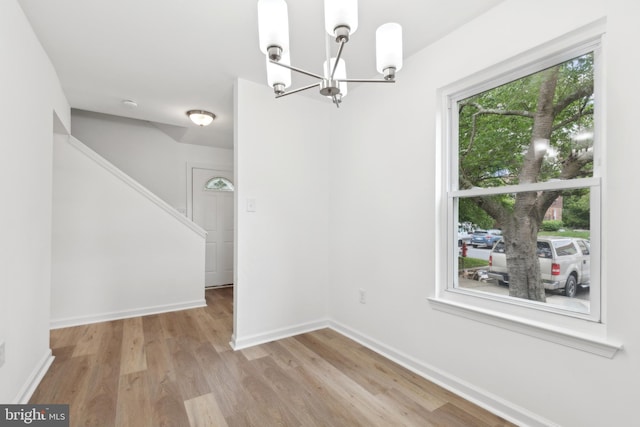 unfurnished dining area featuring a chandelier, wood finished floors, stairs, and baseboards