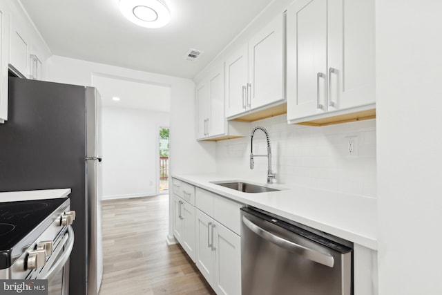 kitchen with appliances with stainless steel finishes, a sink, decorative backsplash, white cabinets, and light wood-type flooring