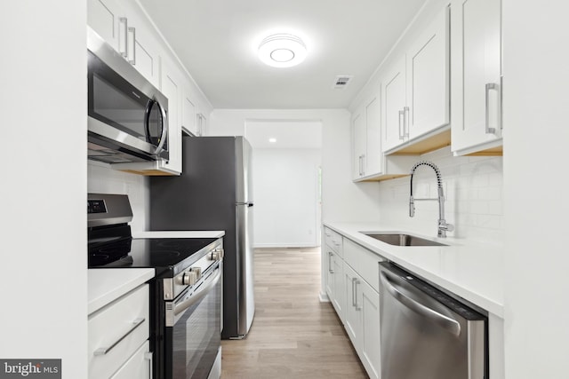 kitchen featuring appliances with stainless steel finishes, a sink, light wood-style floors, tasteful backsplash, and light countertops