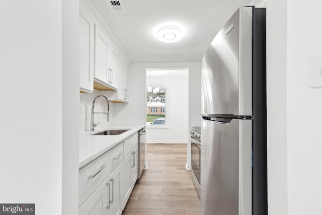 kitchen with appliances with stainless steel finishes, a sink, light wood finished floors, light countertops, and white cabinets