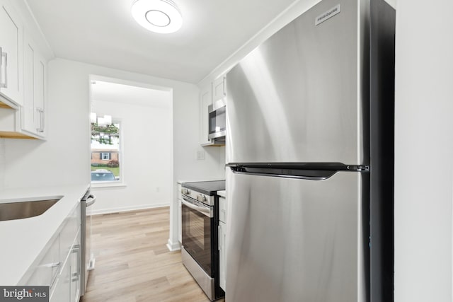 kitchen featuring stainless steel appliances, white cabinets, light wood finished floors, light countertops, and baseboards