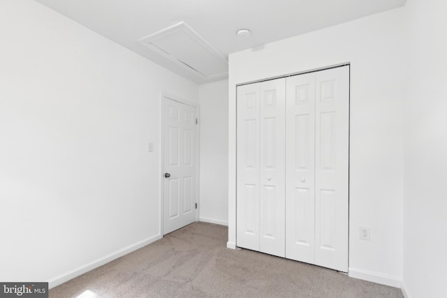 unfurnished bedroom with carpet floors, baseboards, a closet, and attic access