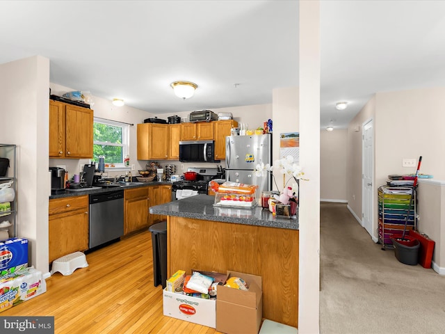 kitchen featuring brown cabinetry, a peninsula, dark countertops, a sink, and appliances with stainless steel finishes