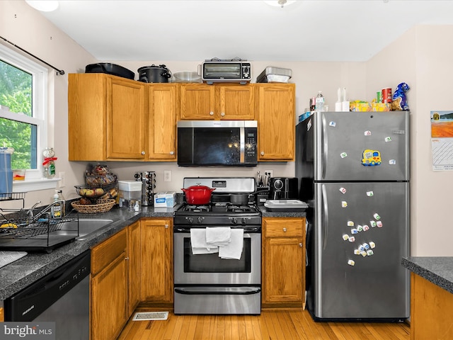 kitchen with dark countertops, appliances with stainless steel finishes, brown cabinets, and light wood finished floors