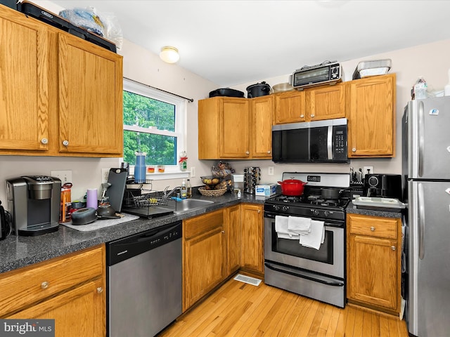kitchen featuring brown cabinetry, dark countertops, light wood-type flooring, a sink, and stainless steel appliances
