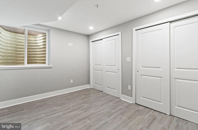 unfurnished bedroom featuring baseboards, recessed lighting, multiple closets, and light wood-type flooring