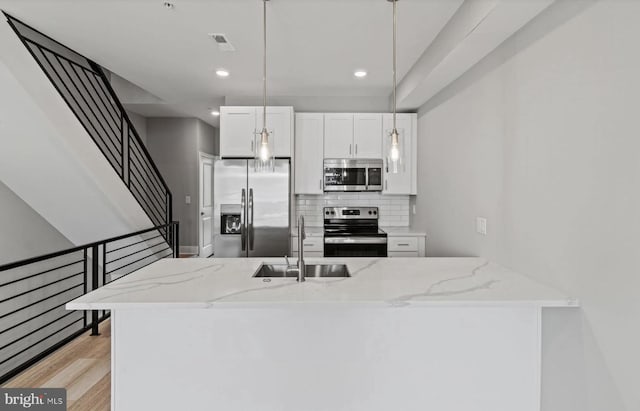 kitchen featuring decorative backsplash, light stone countertops, a sink, white cabinets, and stainless steel appliances