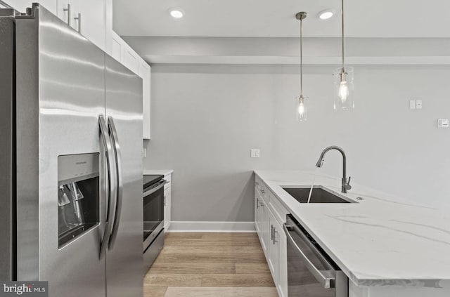 kitchen featuring appliances with stainless steel finishes, a sink, light wood-style flooring, a peninsula, and white cabinetry