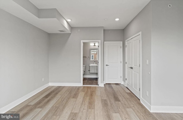 unfurnished bedroom featuring connected bathroom, baseboards, visible vents, and light wood finished floors