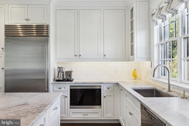 kitchen with a sink, built in appliances, backsplash, and white cabinets