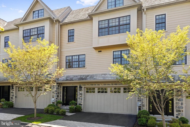 townhome / multi-family property with an attached garage, stone siding, and aphalt driveway