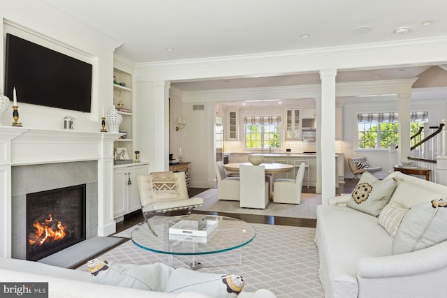 living area with light wood-style floors, ornamental molding, a warm lit fireplace, and a wealth of natural light