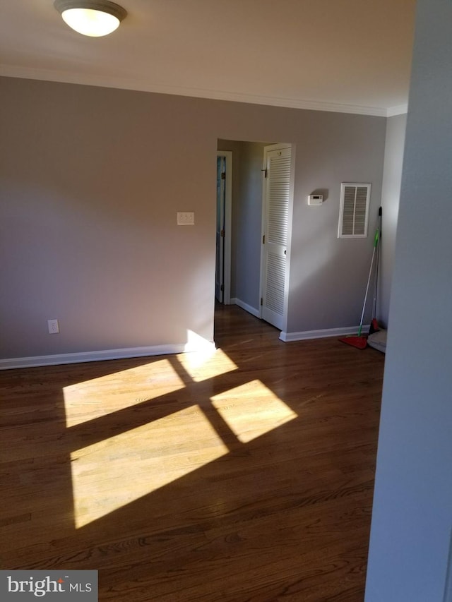 unfurnished room with dark wood-style flooring, baseboards, visible vents, and ornamental molding