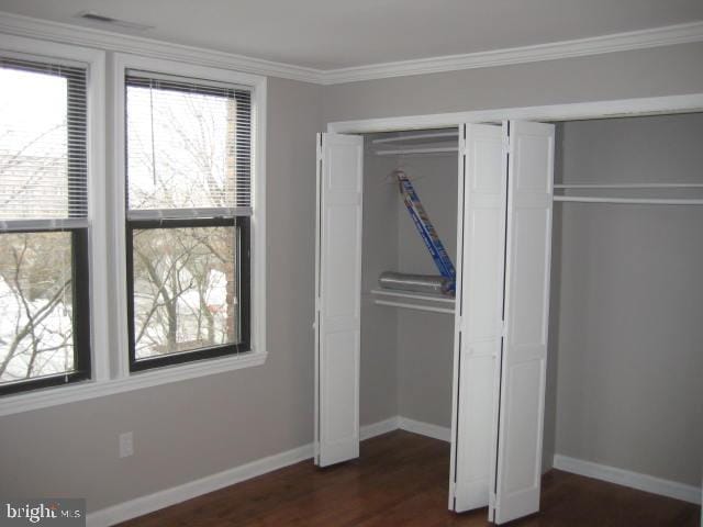 unfurnished bedroom with crown molding, baseboards, a closet, and dark wood-style flooring