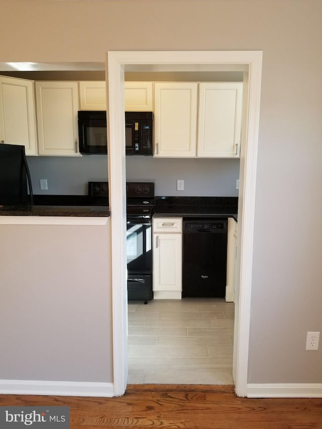 kitchen with dark countertops, light wood-style floors, baseboards, white cabinets, and black appliances