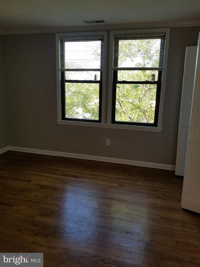 spare room featuring crown molding, baseboards, and dark wood-style floors