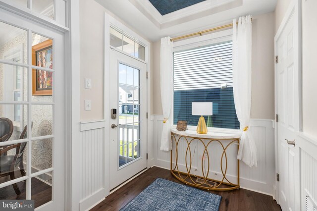 doorway to outside with a decorative wall, dark wood finished floors, a raised ceiling, and a wainscoted wall