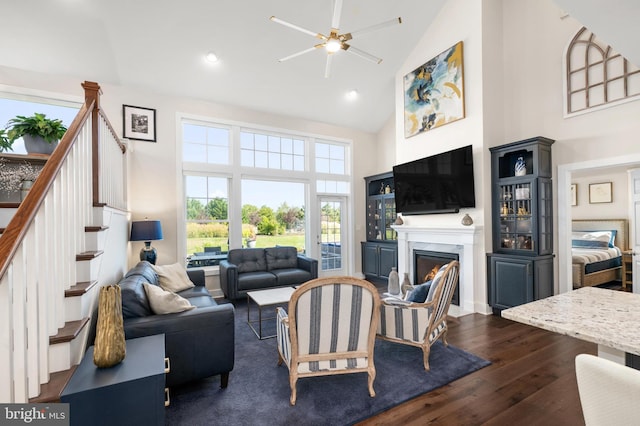 living room with ceiling fan, a fireplace, high vaulted ceiling, stairs, and dark wood-type flooring