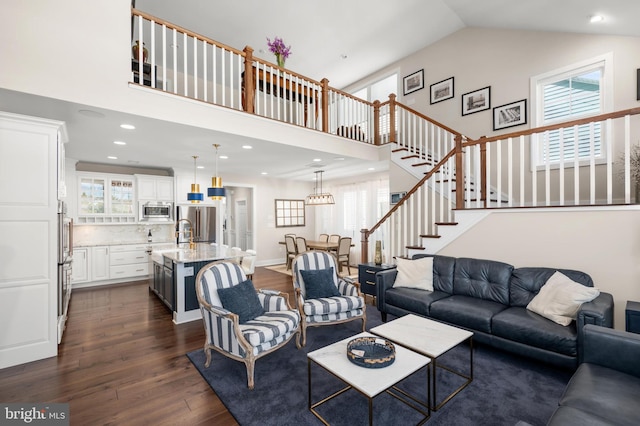 living area with high vaulted ceiling, dark wood finished floors, a healthy amount of sunlight, and stairway