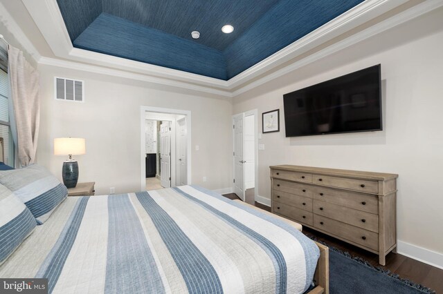 bedroom with a tray ceiling, visible vents, baseboards, and wood finished floors