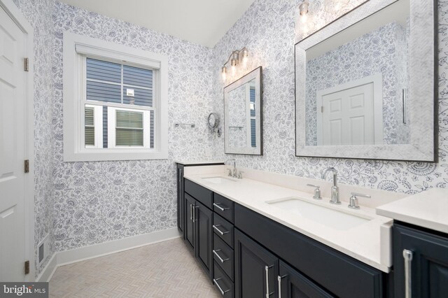 bathroom featuring double vanity, baseboards, wallpapered walls, and a sink