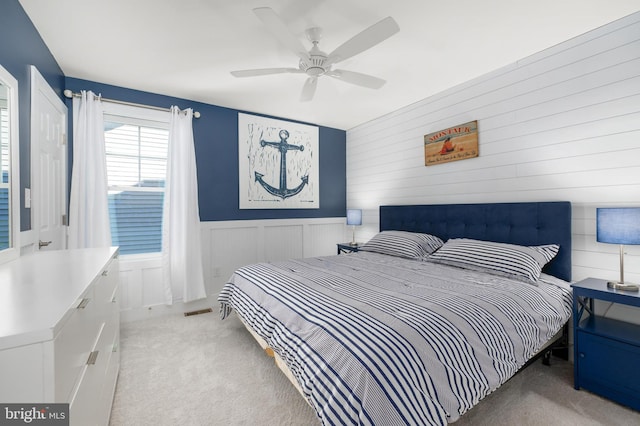 bedroom with visible vents, ceiling fan, a wainscoted wall, and light carpet