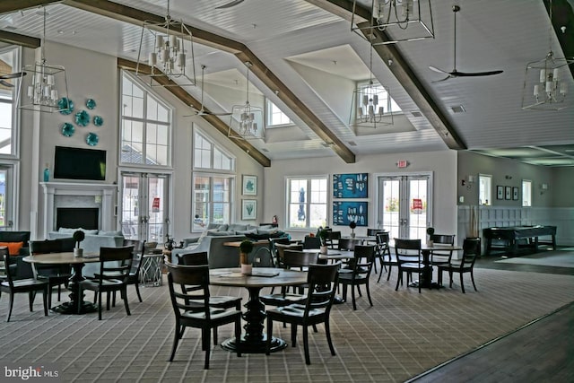carpeted dining area with a towering ceiling, beam ceiling, a wainscoted wall, a chandelier, and french doors