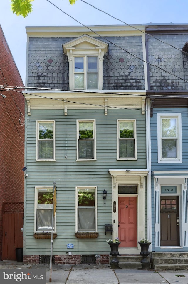 view of front of home featuring fence, entry steps, and mansard roof