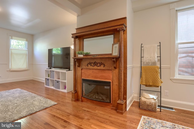 living room featuring a glass covered fireplace, baseboards, wood finished floors, and visible vents