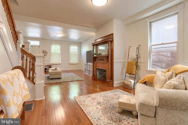 living room with visible vents, a glass covered fireplace, baseboards, stairway, and hardwood / wood-style flooring