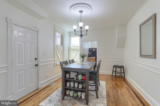 dining area featuring crown molding, an inviting chandelier, baseboards, wood finished floors, and visible vents
