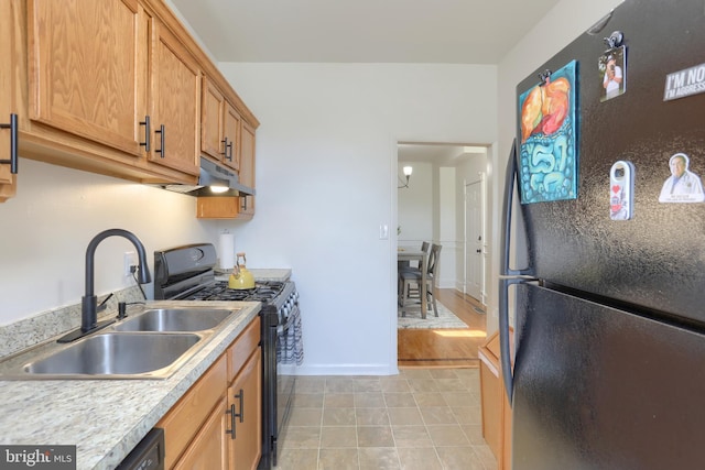 kitchen with a sink, light countertops, baseboards, black appliances, and under cabinet range hood