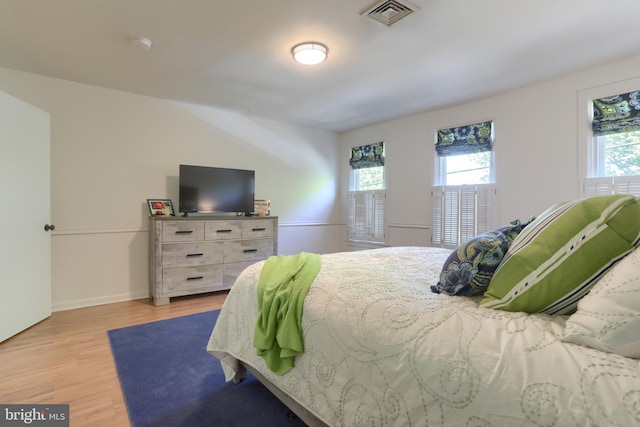bedroom featuring baseboards, multiple windows, wood finished floors, and visible vents