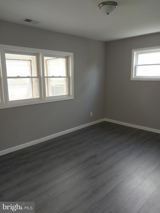 spare room featuring visible vents, dark wood-style flooring, and baseboards