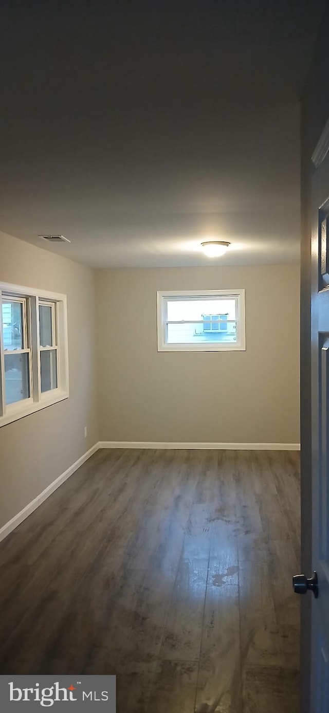 empty room with baseboards, dark wood-style flooring, and visible vents