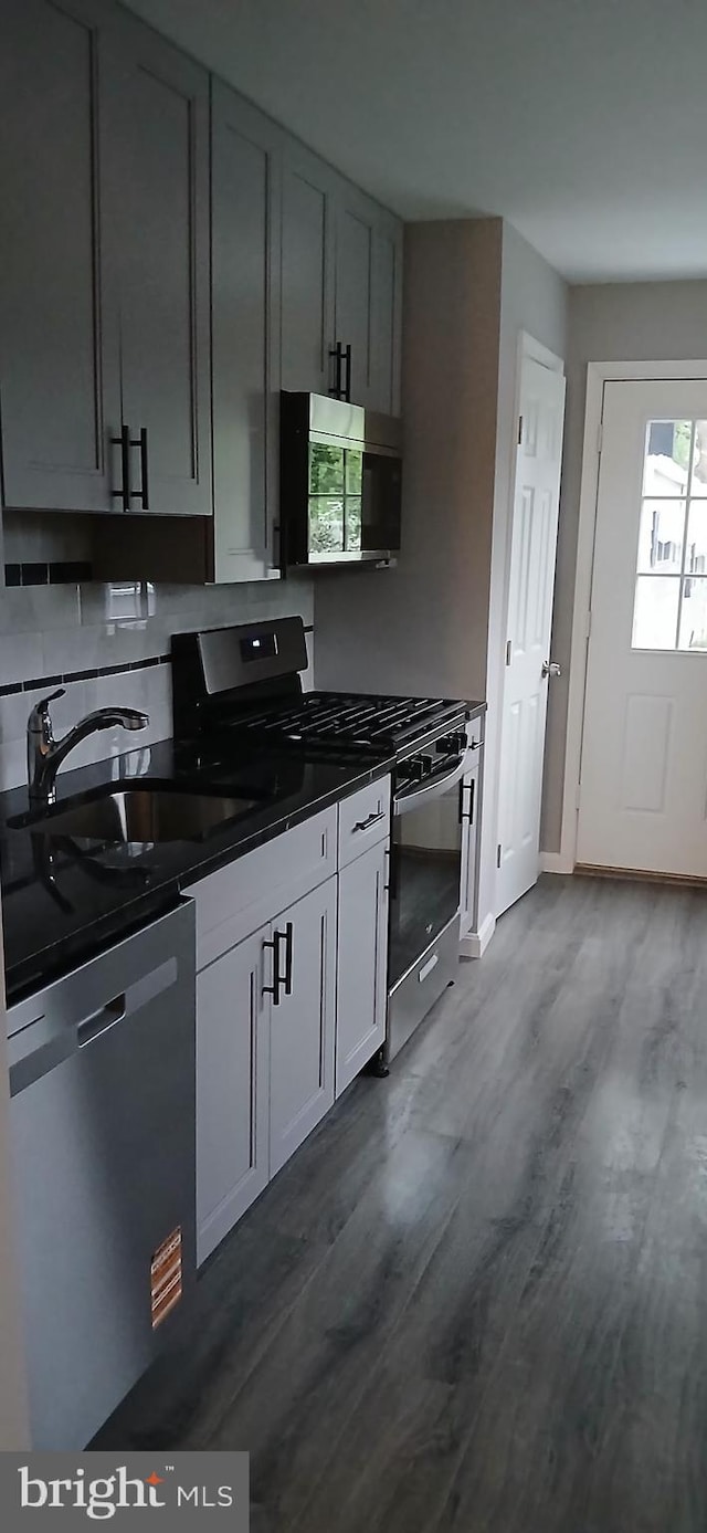 kitchen with decorative backsplash, dark countertops, a sink, dark wood finished floors, and stainless steel appliances