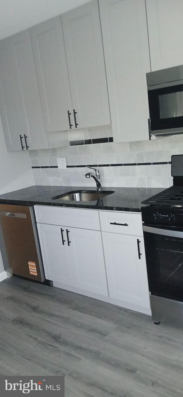 kitchen with a sink, range with gas stovetop, stainless steel microwave, and white cabinetry