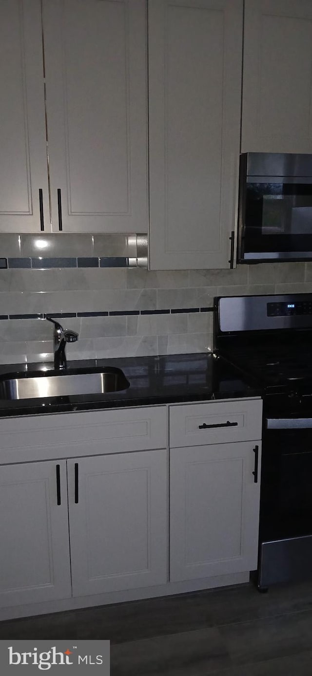 kitchen with backsplash, dark countertops, stainless steel range with electric cooktop, a sink, and white cabinetry