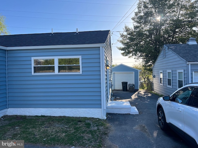 view of side of home with driveway, an outbuilding, roof with shingles, and a garage