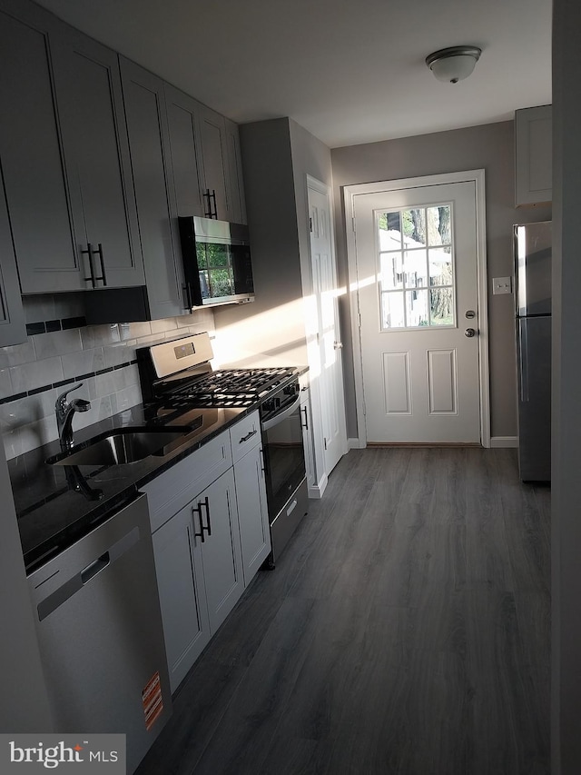 kitchen featuring dark wood-style flooring, dark countertops, appliances with stainless steel finishes, a sink, and backsplash