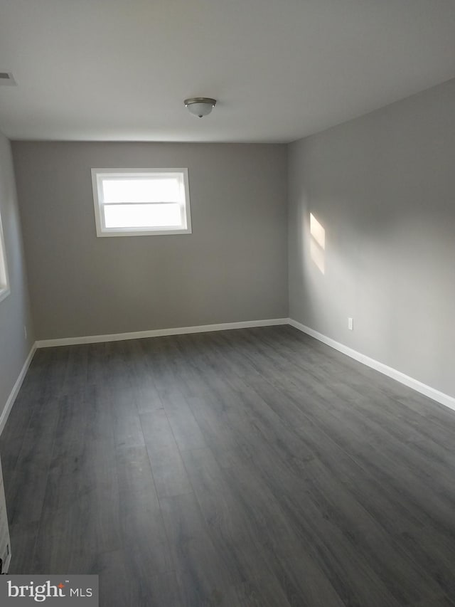 empty room with baseboards and dark wood-type flooring