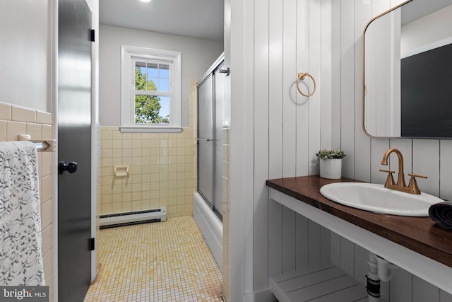 bathroom featuring wainscoting, a sink, baseboard heating, tile walls, and combined bath / shower with glass door