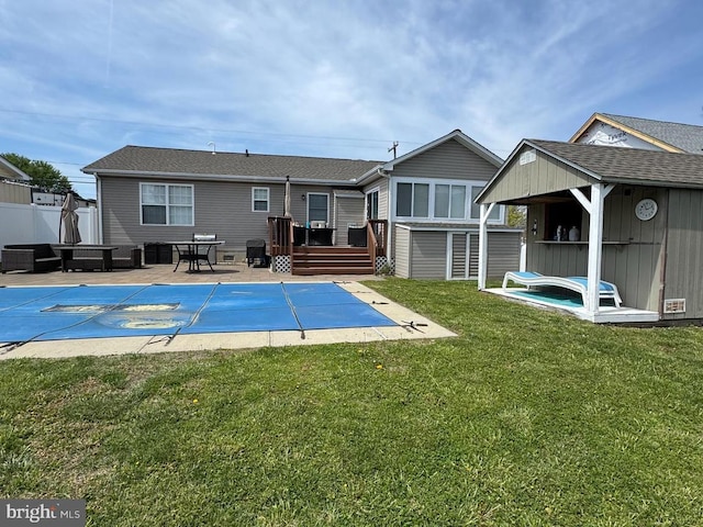 rear view of house featuring an outdoor structure, a deck, a shed, a fenced in pool, and a lawn