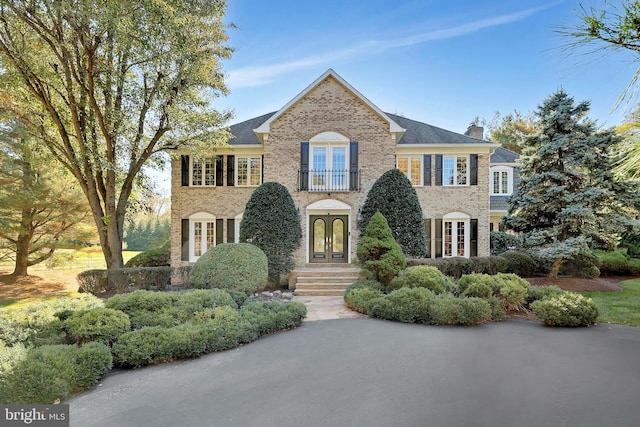 view of front of property with brick siding, french doors, stone siding, and a chimney