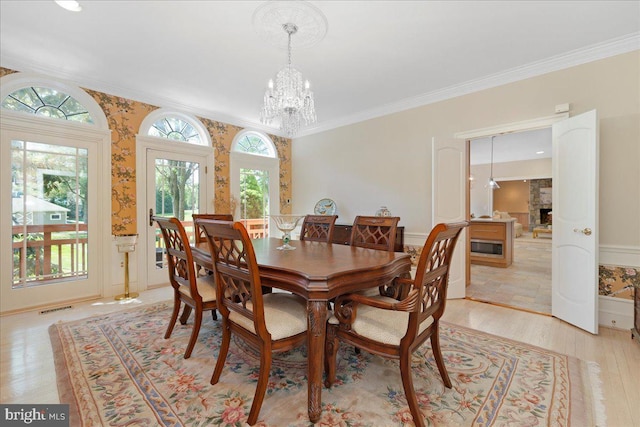 dining space with visible vents, crown molding, an inviting chandelier, a fireplace, and light wood-type flooring