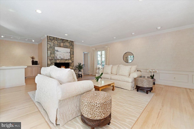 living room with ornamental molding, a wainscoted wall, light wood finished floors, and a fireplace
