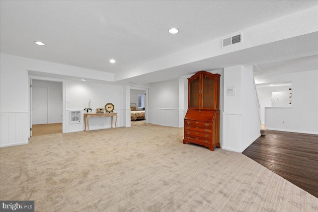 finished below grade area with visible vents, wood finished floors, recessed lighting, a wainscoted wall, and carpet